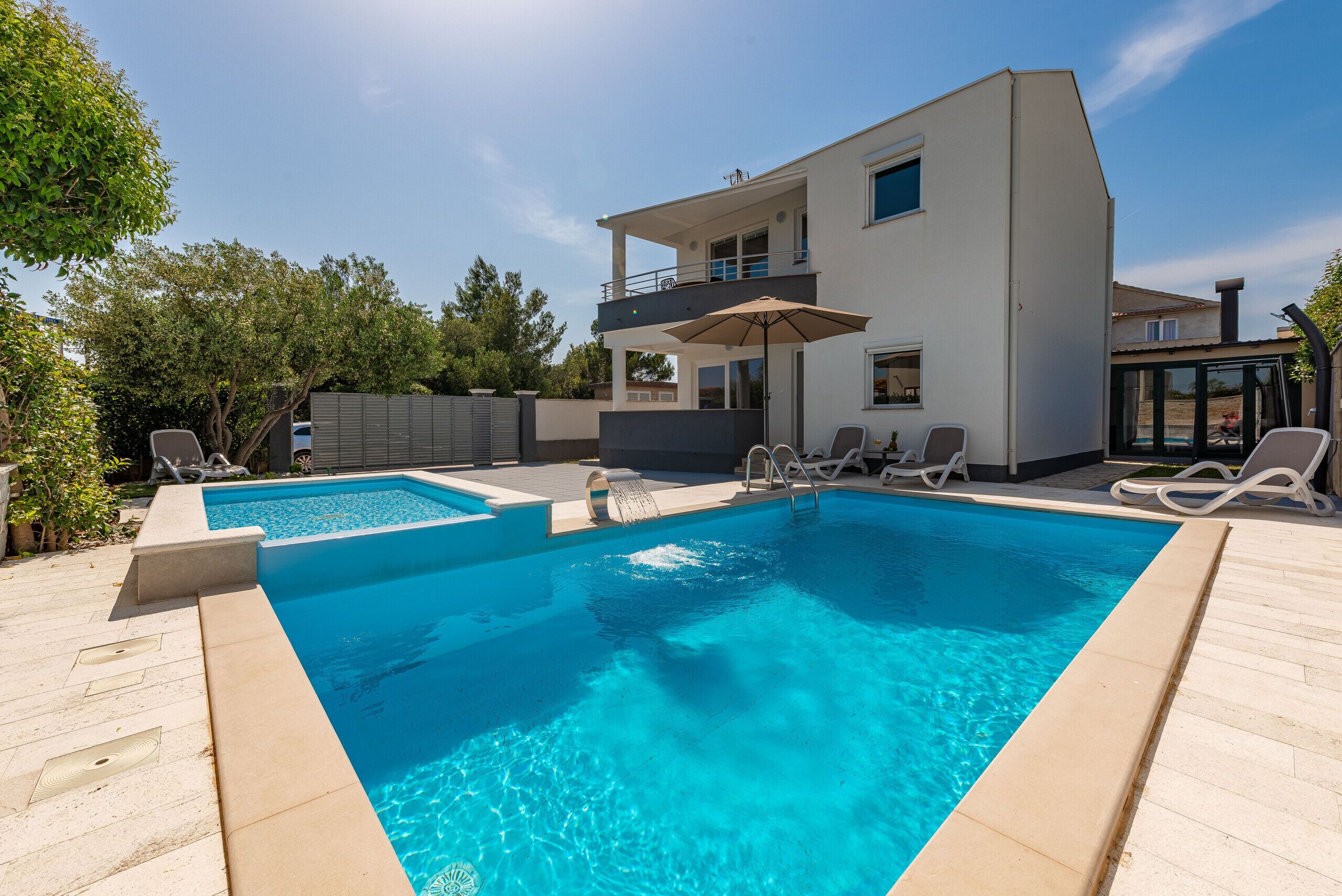 A modern two-story house with a swimming pool, outdoor seating, and a balcony.