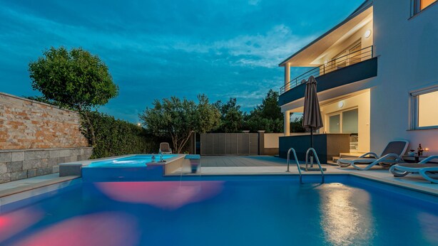 A modern outdoor pool area with a hot tub, lounge chairs, and a two-story building with balconies. - Villa Julija (Sukosan)