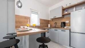 A modern kitchen with a wooden island, two black bar stools, a stainless steel refrigerator, and a window with a view. - Villa Julija (Sukosan)