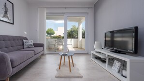 A modern living room with a grey sofa, a flat-screen TV on a white stand, and a glass door leading to an outdoor patio. - Villa Julija (Sukosan)