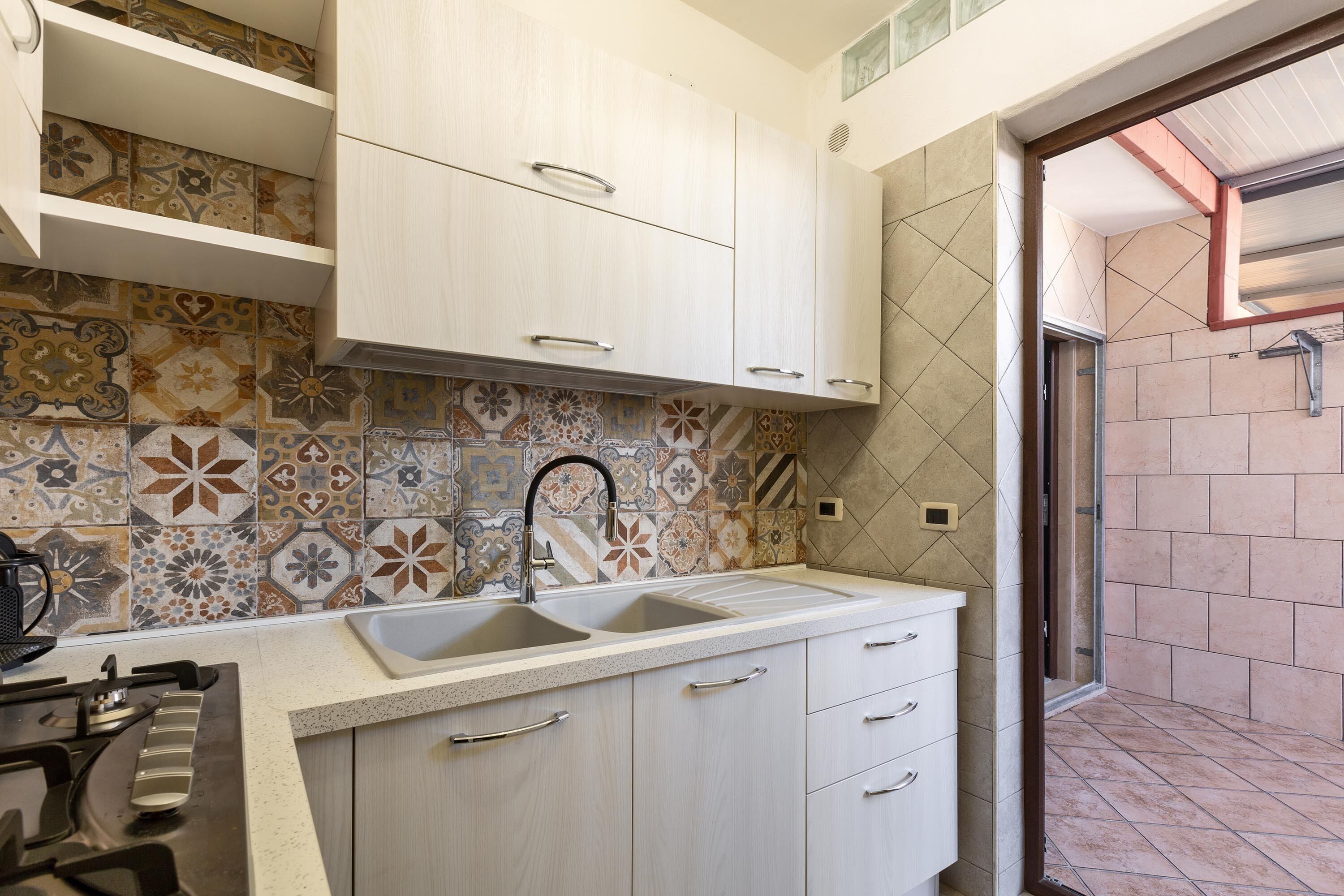 A kitchen with a double sink, white cabinets, and a patterned backsplash.