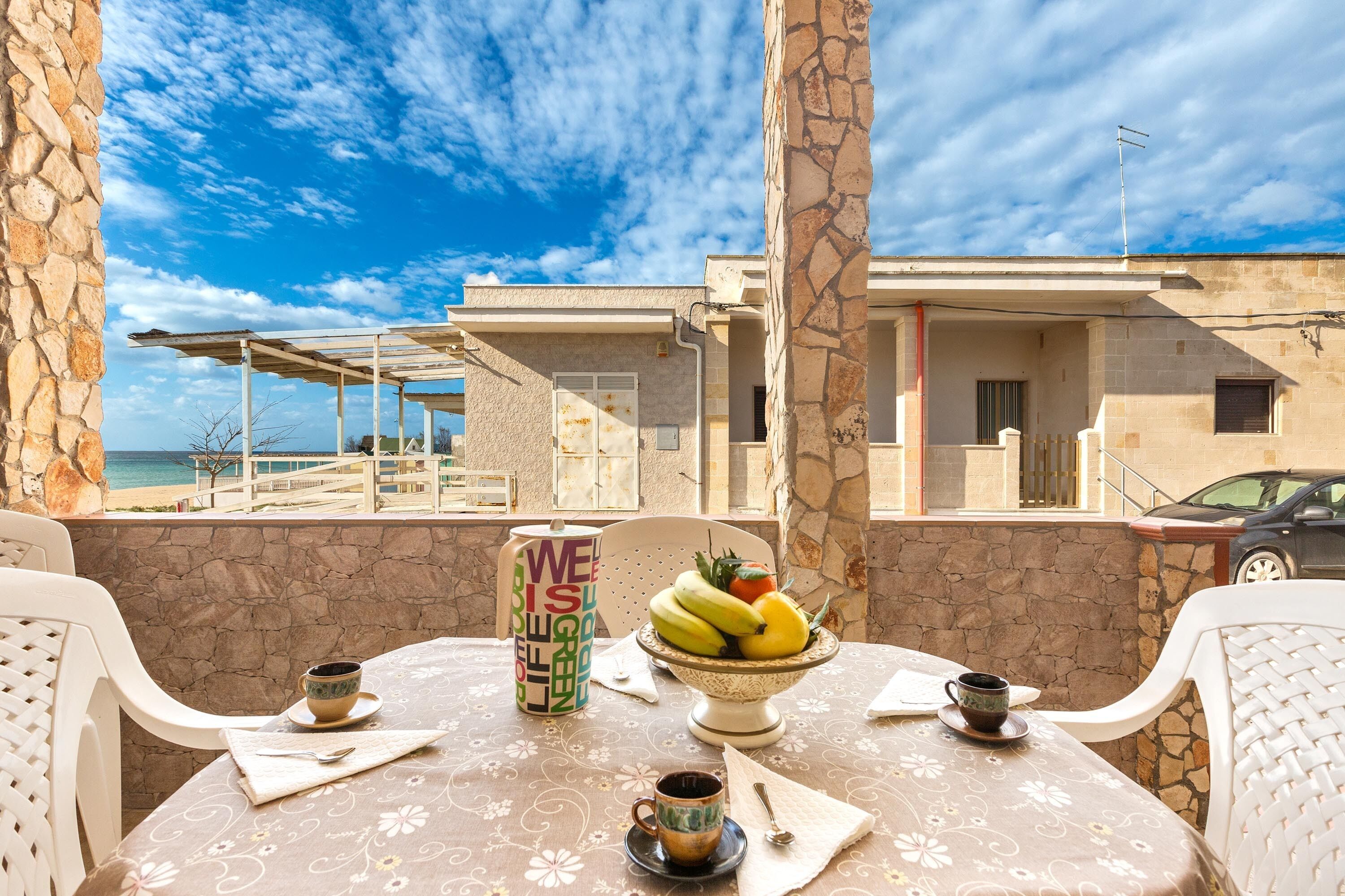 Una mesa de comedor con vista al mar, una pared de piedra y un edificio al fondo.