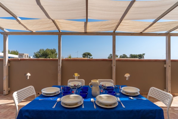 An outdoor dining area with a table set for four, covered by a canopy, and a view of the surrounding landscape.