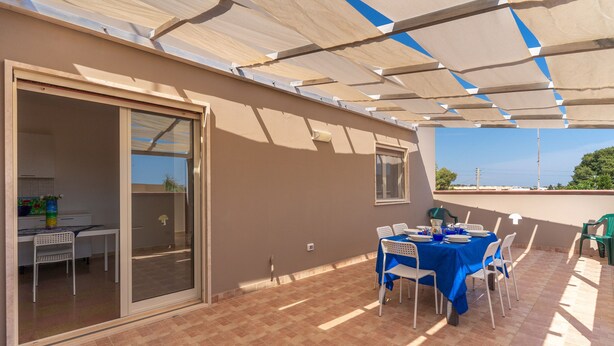 Eine überdachte Terrasse mit Esstisch, eine Glastür zum Raum hin und Blick zum Himmel.