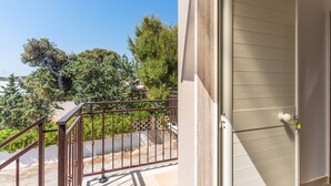 Ein Balkon mit Metallgeländer, der auf einen befestigten Bereich und Bäume blickt.