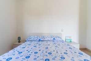 A bed with a floral bedspread, a bedside lamp, and a small table with a painting.