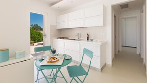 Une cuisine moderne avec des meubles blancs, un coin repas avec des chaises de couleur turquoise et une vue sur la verdure à l’extérieur.