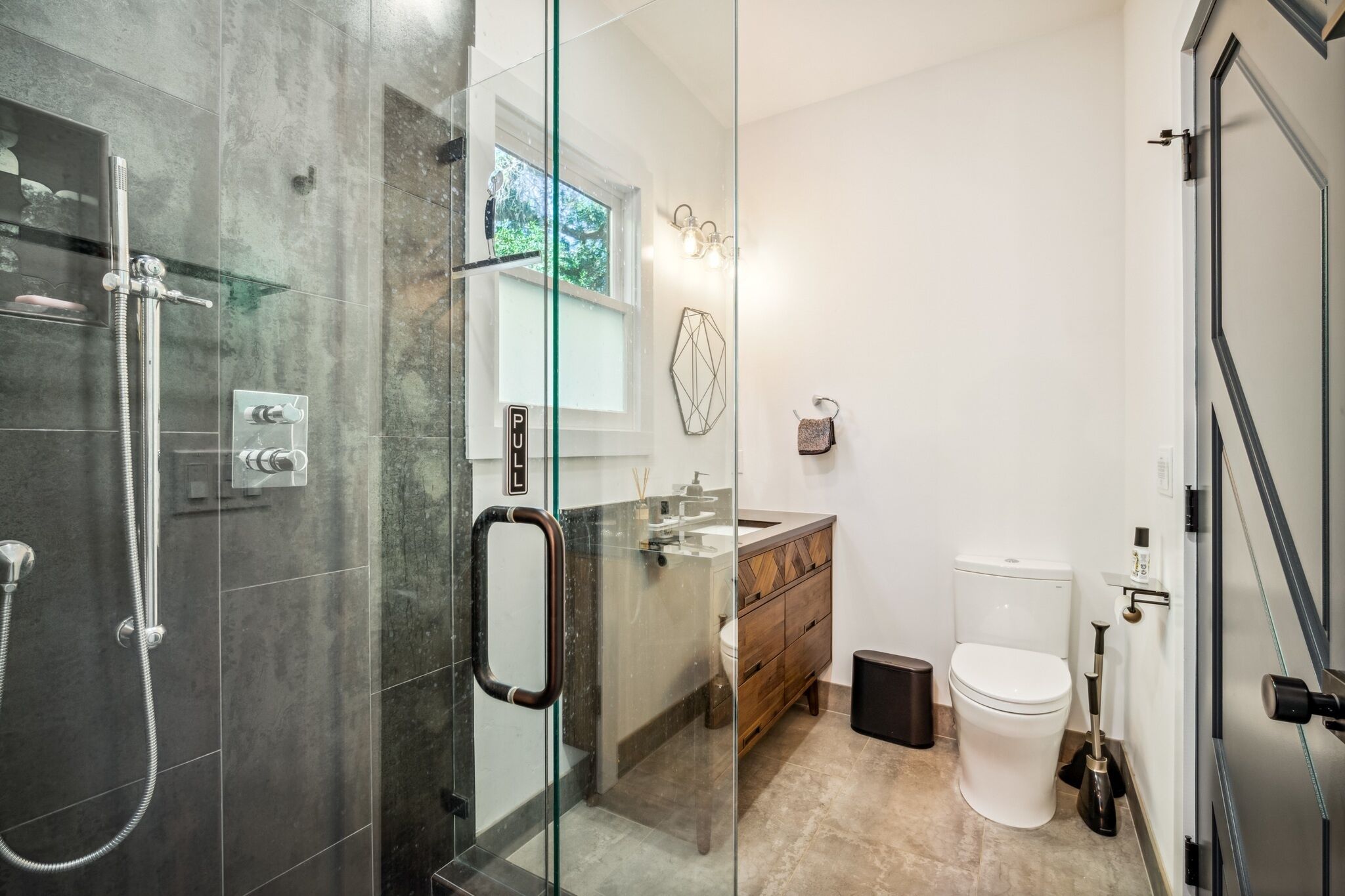 Et moderne badeværelse med et glasbadeværelse, et trækommode og et hvidt toilet.
