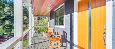A wooden deck with outdoor furniture, a sliding glass door, and a view of the surrounding greenery.