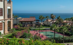 A resort with a tennis court, palm trees, and ocean views.