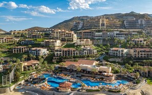Un resort con varias edificaciones, una piscina central y un paisaje montañoso de fondo.