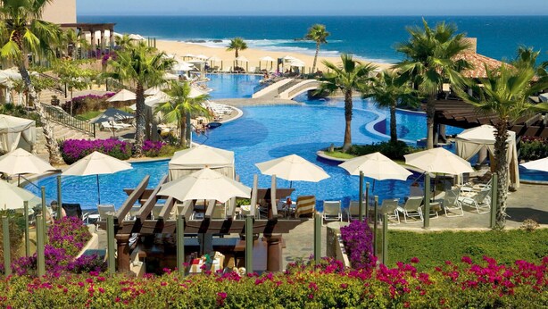 Un complexe hôtelier doté d’une grande piscine, d’un accès à la plage et de palmiers.