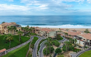 Un resort costero con varias edificaciones, palmeras y un camino curvo que lleva a la playa.
