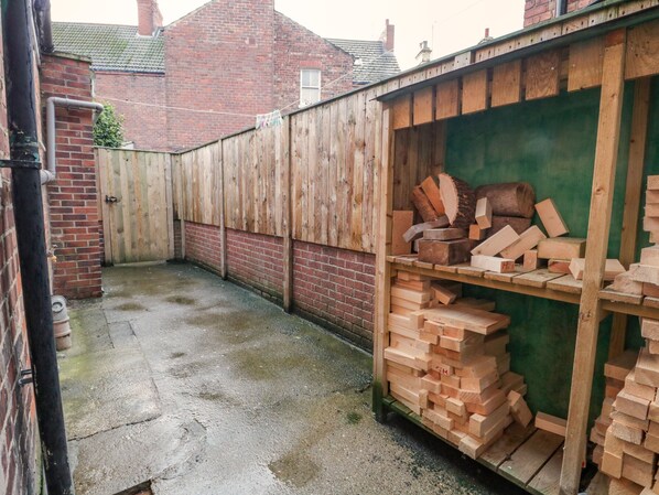 A wooden shed with stacks of firewood and a brick wall.