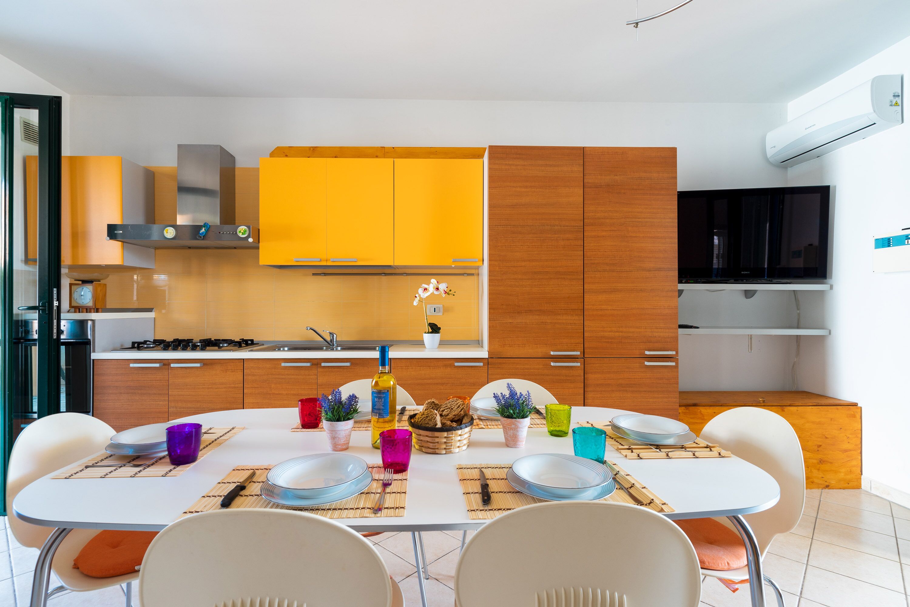 Een moderne keuken met gele kastjes, een inbouwfornuis en een eethoek met een witte tafel en stoelen.