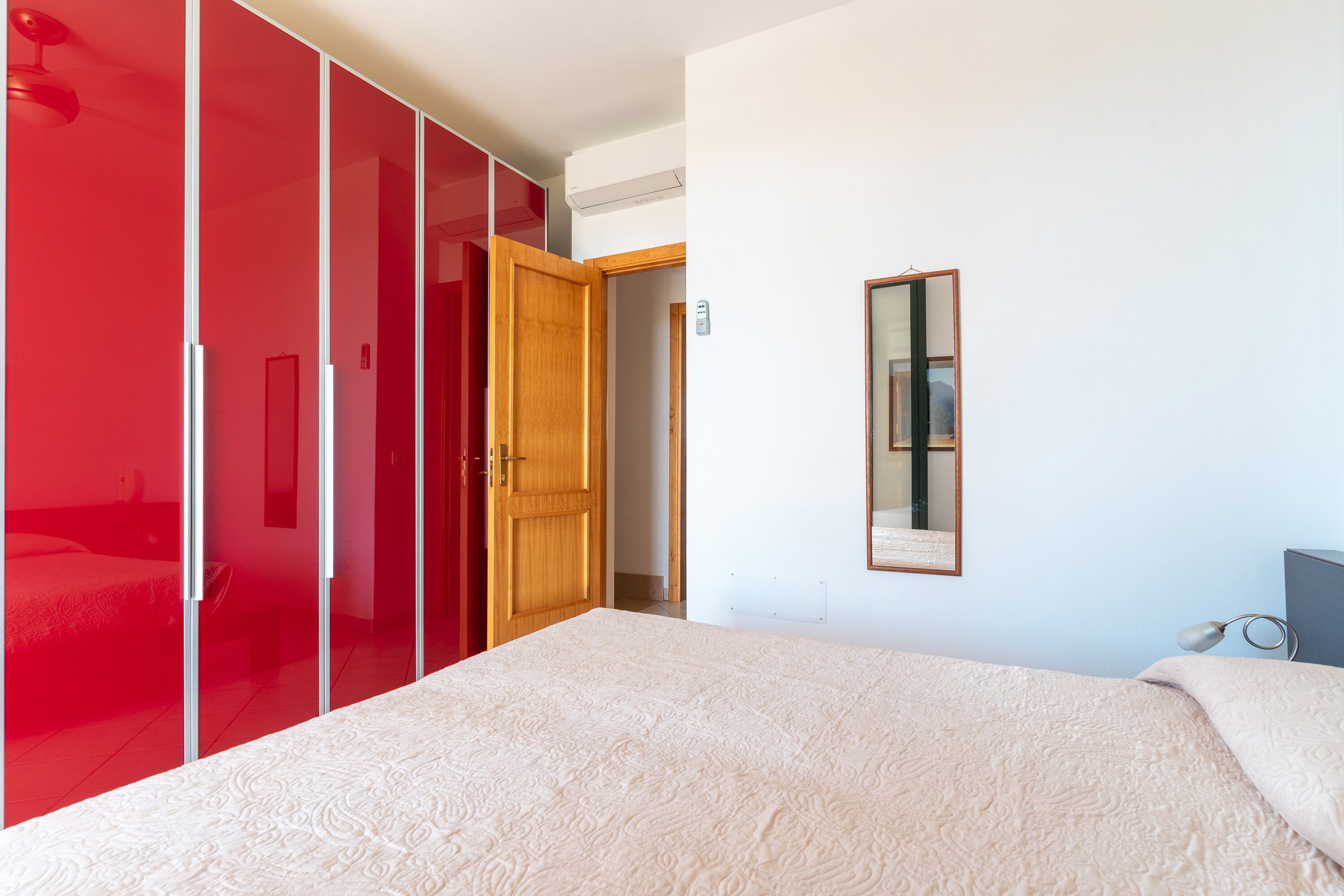 Ein Schlafzimmer mit einem Bett, einem roten Kleiderschrank und einem Spiegel an der Wand.