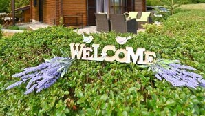 Een houten chalet met een balkon, omringd door weelderige begroeiing en een 'Welcome' bord.
