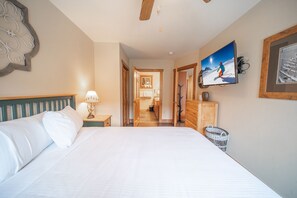 A bedroom with a bed, a television mounted on the wall, and a hallway leading to a bathroom. - Red Hawk Lodge 2270 (Keystone)