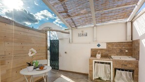 Een zonnig terras met een houten tafel, een bloempot en een klein zithoekje.