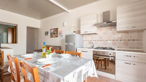 A modern kitchen with a dining area, featuring a table set for four, a refrigerator, a stove, and a sink. - 3021 Villa Seremar by Barbarhouse (Trepuzzi)