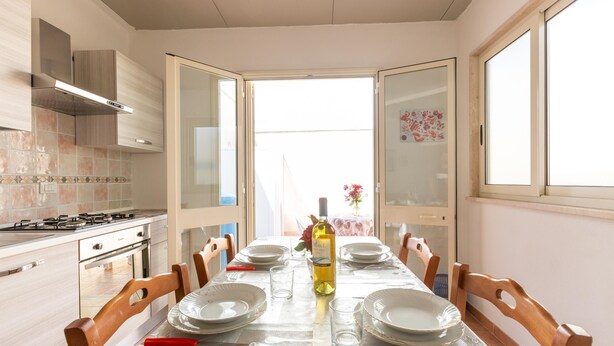 A dining area with a table set for six, a wine bottle, and a view of the outdoors. - 3021 Villa Seremar by Barbarhouse (Trepuzzi)