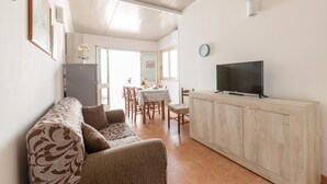 A living room with a sofa, a TV on a wooden cabinet, a dining area with a table and chairs, and a kitchen area with a refrigerator. - 3021 Villa Seremar by Barbarhouse (Trepuzzi)