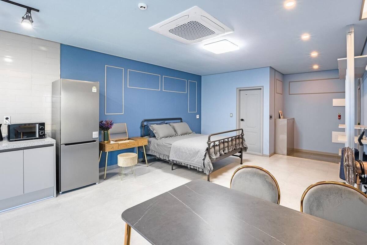 A compact hotel room with a kitchenette, a bed, a dining table, and a bathroom.