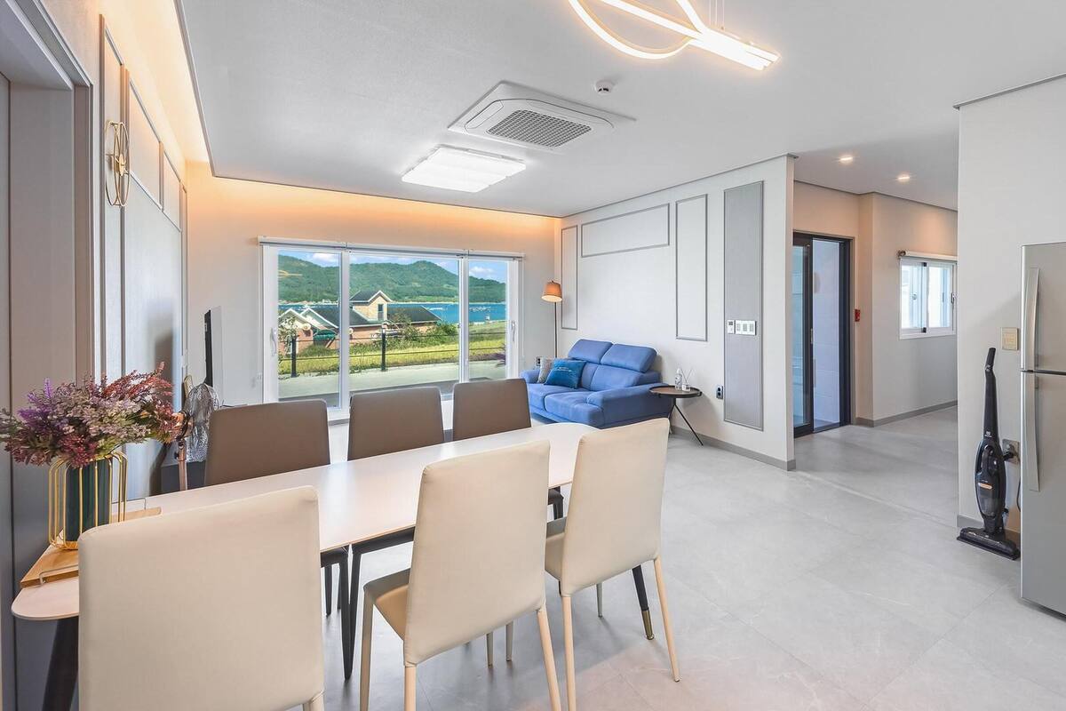 A modern kitchen with a dining area, a blue sofa, and a large window offering a view of the outdoors.