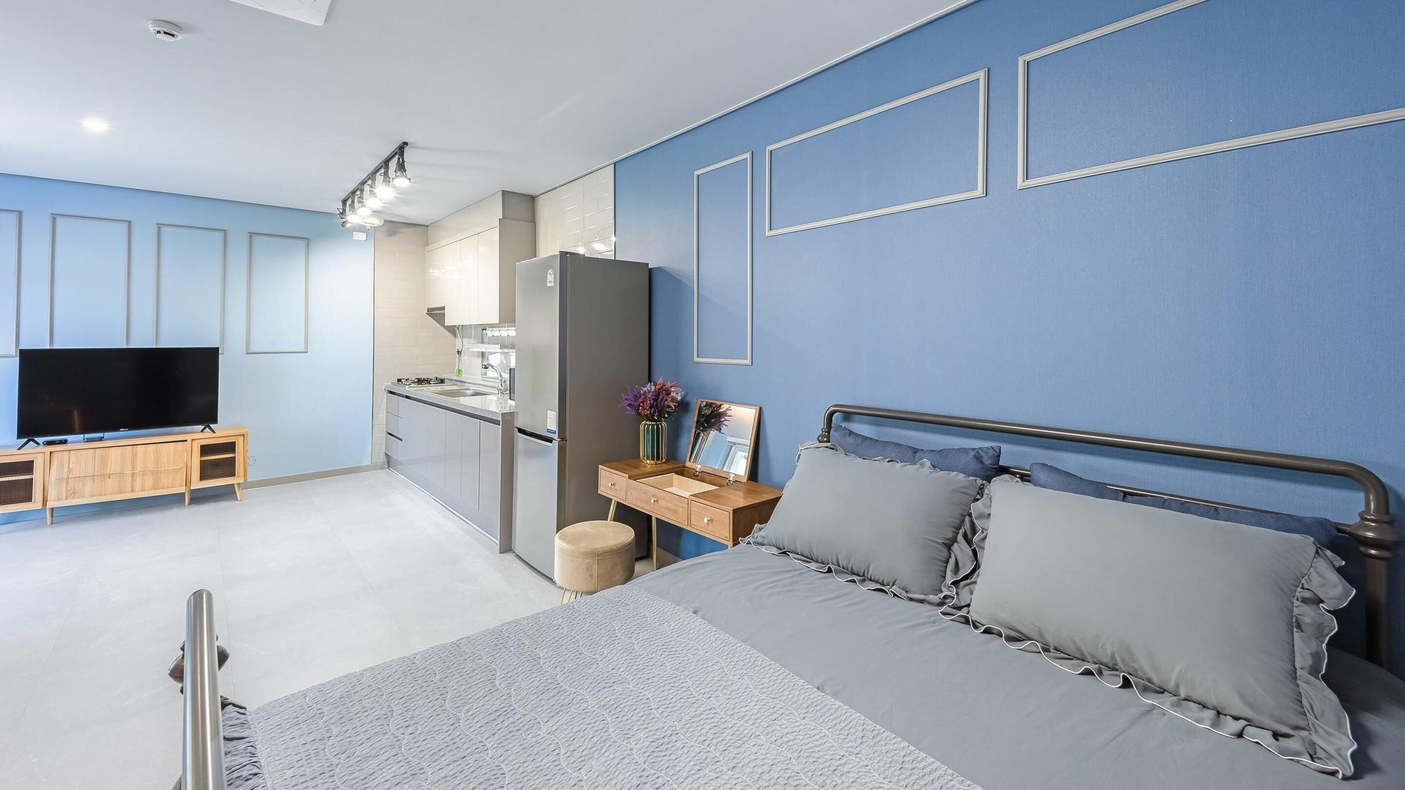 Un dormitorio moderno con cama, mesita de noche, televisor y kitchenette.