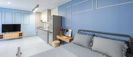Un dormitorio moderno con cama, mesita de noche, televisor y kitchenette.
