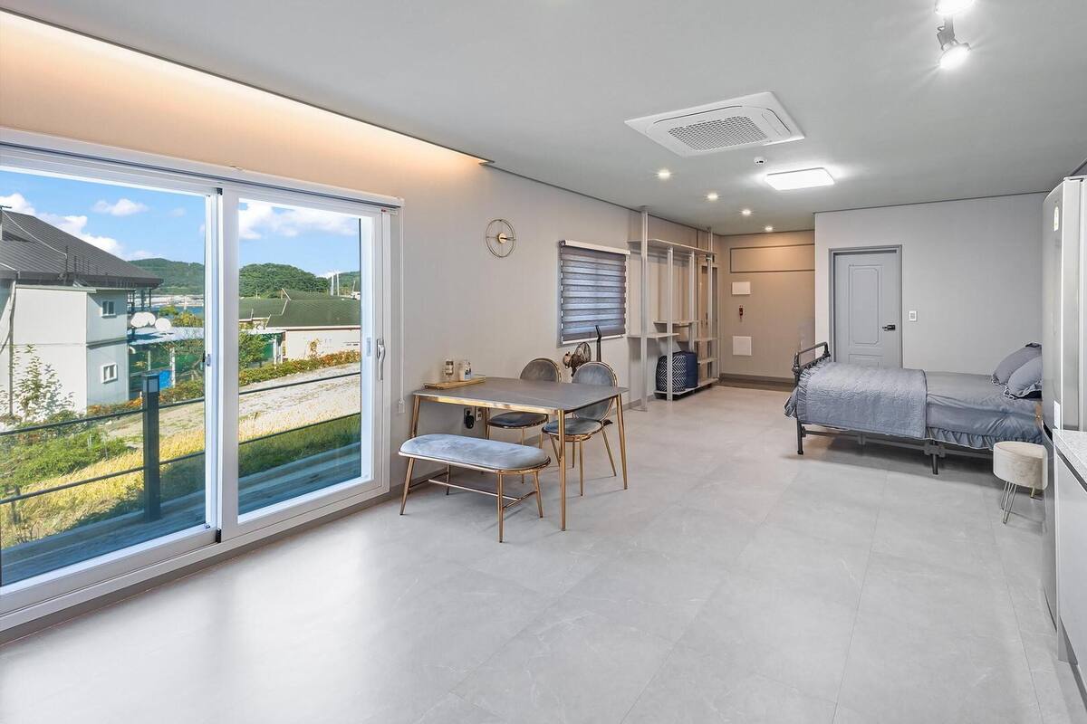 A modern, well-lit room with a dining area, a bed, and a kitchenette.
