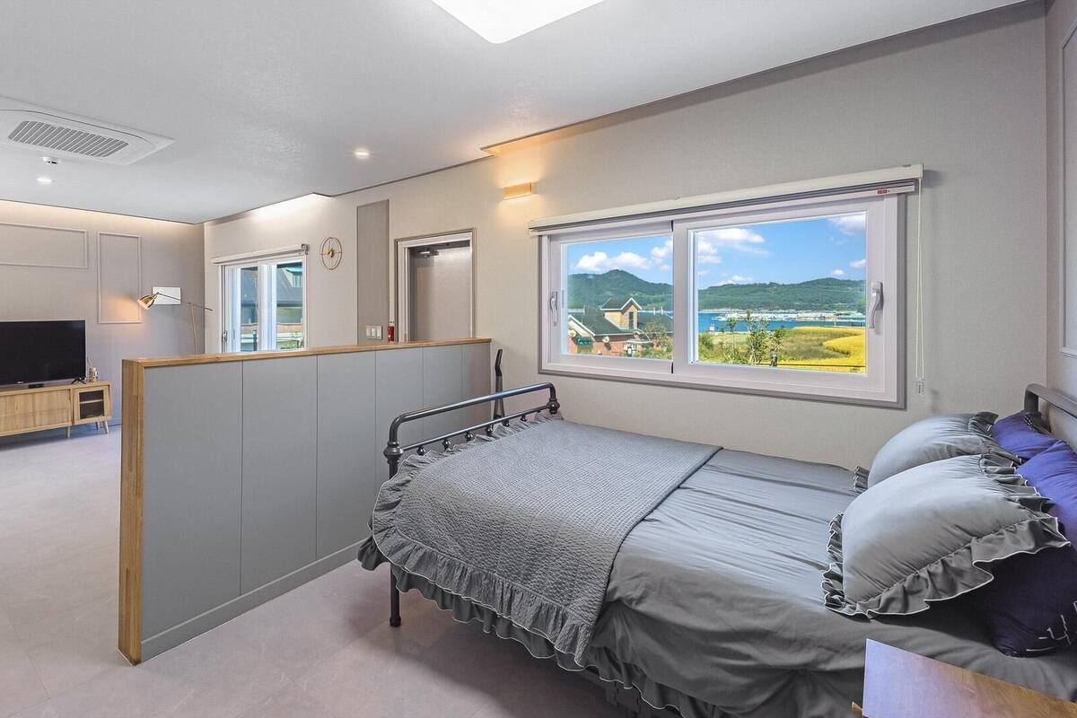 A bedroom with a bed, a TV, a window with a view, and a partition wall.