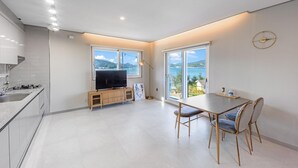 Une cuisine moderne dotée d’une cuisinière intégrée, un coin repas avec une table et des chaises, et de grandes fenêtres offrant une vue sur la mer.