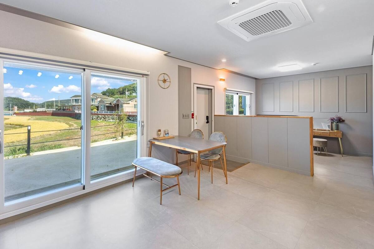 A modern interior with a dining area, a small seating space, and a view of a residential area.
