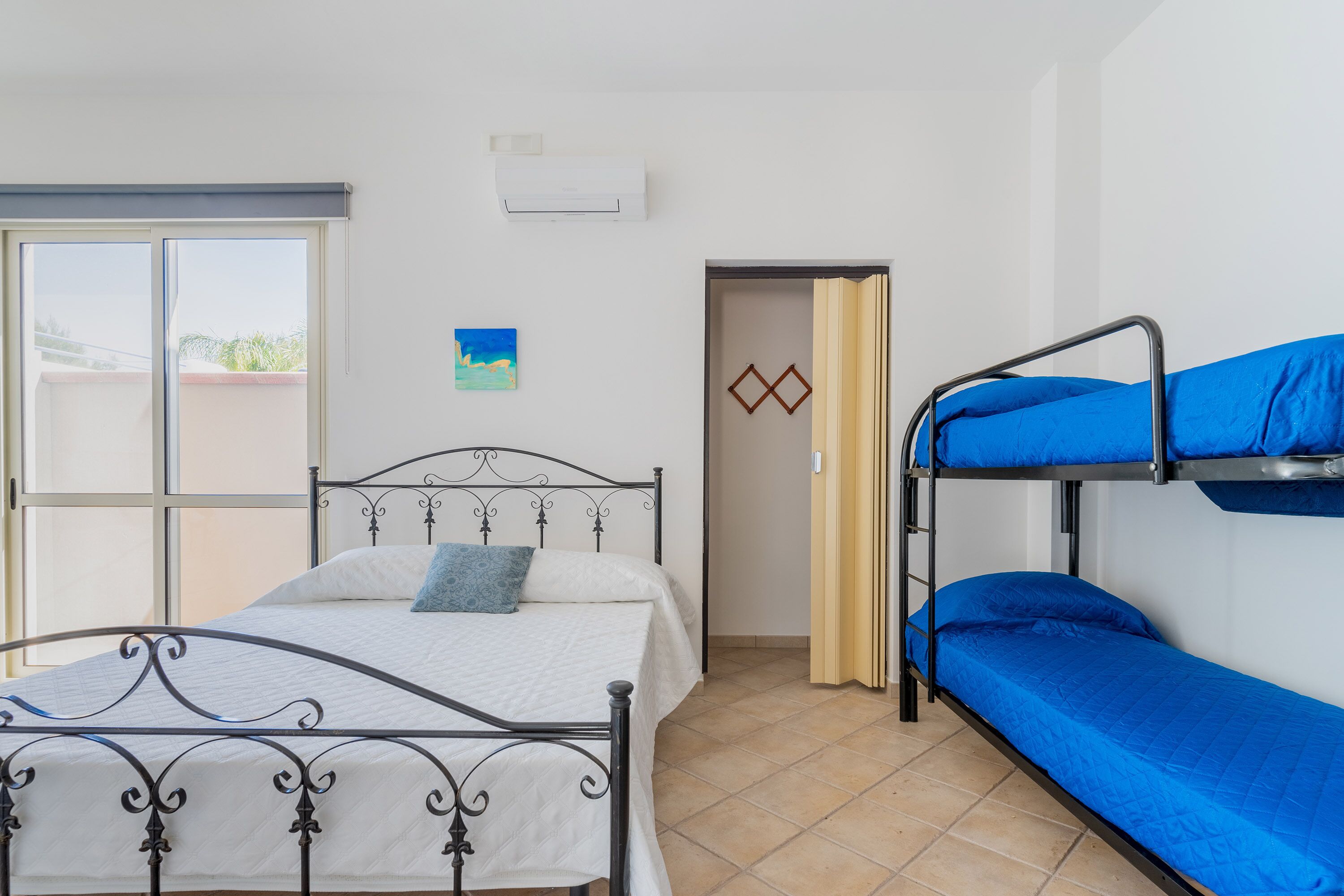 A room with a bed, a bunk bed, a window, and a door.