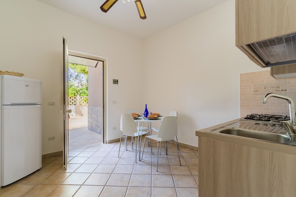 A compact kitchen with a white refrigerator, a dining table with chairs, a sink, and a stove.