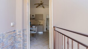 A hallway leading to a kitchen with a dining area, a ceiling fan, and a stone wall. - 2952 Residence Flamingo - Appartamento Piccolo by Barbarhouse (Manduria)