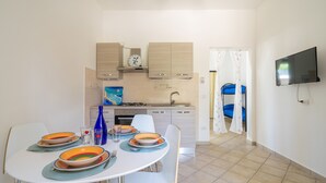 A compact kitchen with modern appliances, a dining area with a table set for four, and a TV mounted on the wall. - 2952 Residence Flamingo - Appartamento Piccolo by Barbarhouse (Manduria)