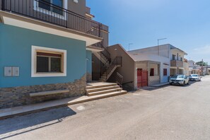 A residential street with a blue house featuring a stone facade, a red gate, and a staircase leading to a balcony. - 2952 Residence Flamingo - Appartamento Piccolo by Barbarhouse (Manduria)