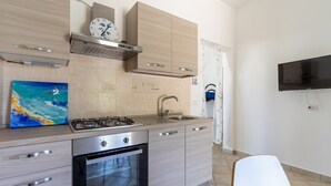 A modern kitchen with a gas stove, oven, and stainless steel appliances. There is a painting on the counter and a flat-screen TV mounted on the wall. - 2952 Residence Flamingo - Appartamento Piccolo by Barbarhouse (Manduria)