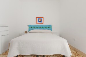 Un dormitorio con una cama, una pared blanca, un cuadro enmarcado y una cortina azul.