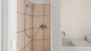 A bathroom with beige tiles, a shower with a handheld showerhead, and a white sink.