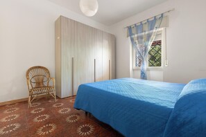 Ein Schlafzimmer mit Bett, Kleiderschrank, Sessel und Fenster mit Vorhängen.