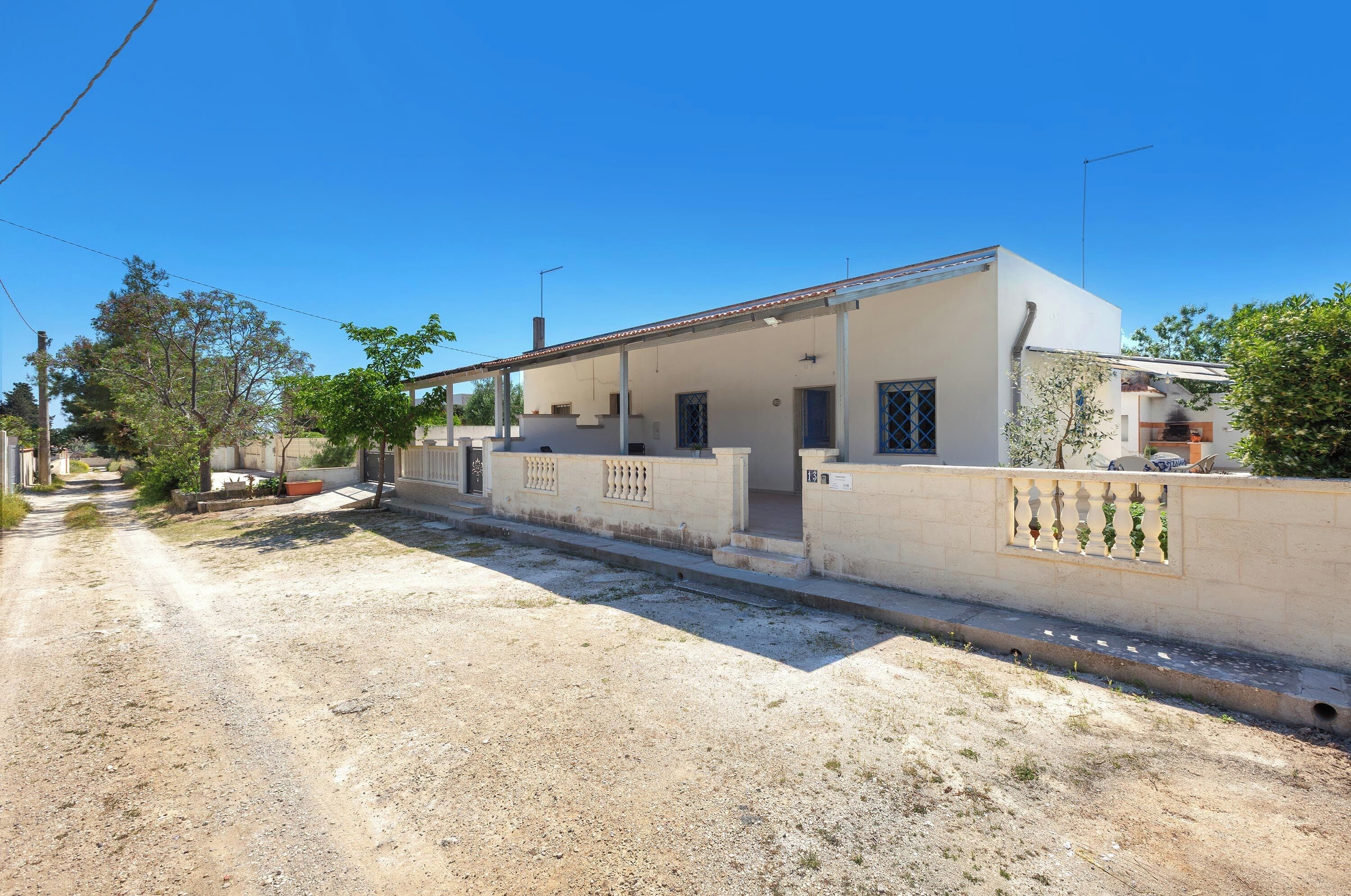 Una casa de dos pisos con un porche cubierto, un jardín pequeño y un camino de tierra.