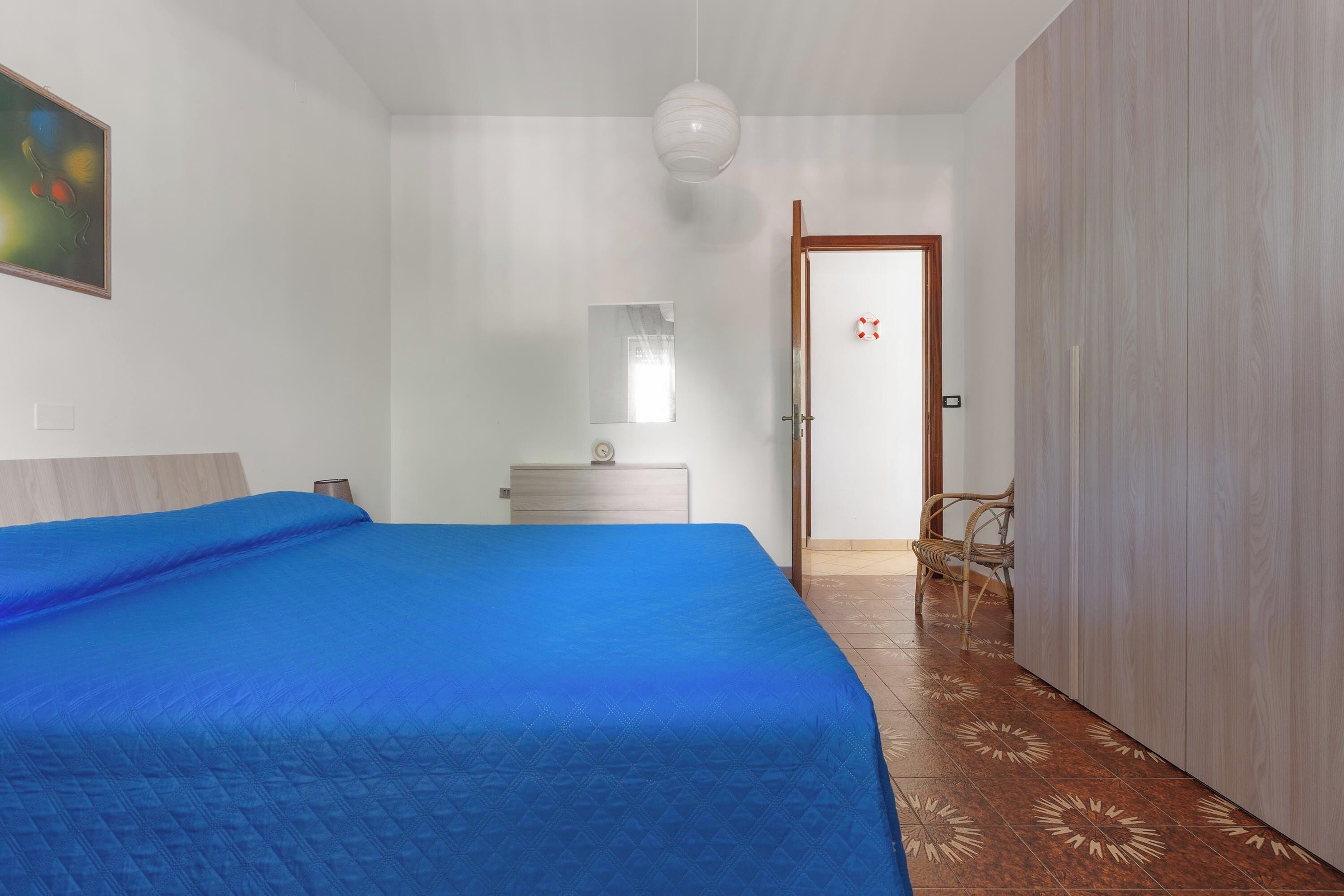 Une chambre à coucher comprenant un lit, une table de chevet, une commode, un miroir, une porte et une chaise.