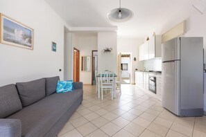 Ein modernes Wohnzimmer mit grauem Sofa, einem Esstisch und einer Küchenzeile mit Kühlschrank.