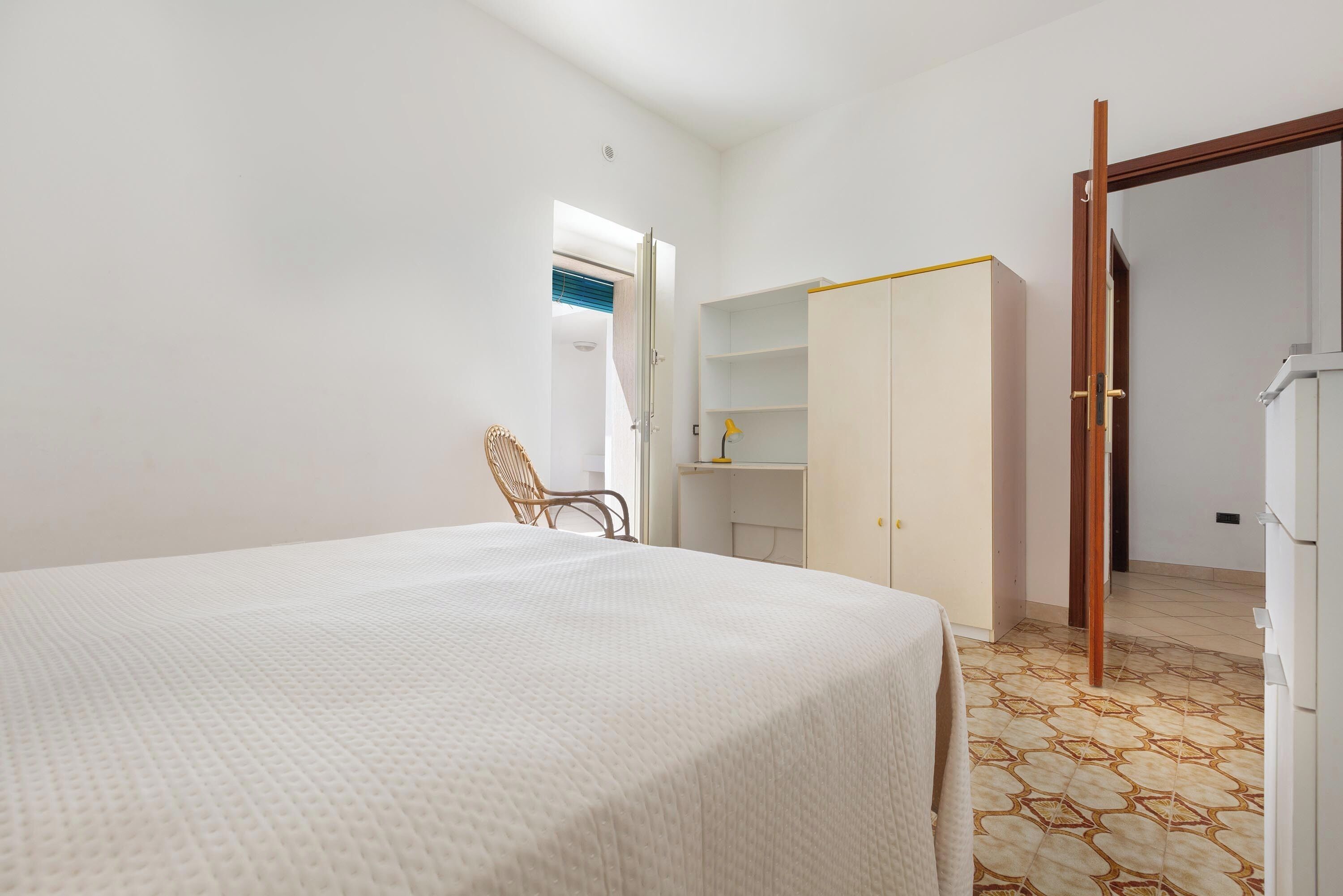 Een slaapkamer met een bed, een stoel, een kledingkast en een deur die naar een andere kamer leidt.
