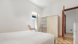 A bedroom with a bed, a chair, a wardrobe, and a door leading to another room.