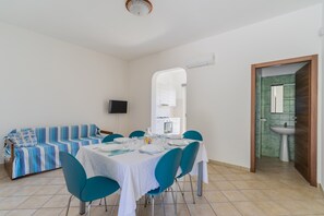 A dining area with a table set for four, a sofa, and a bathroom visible through an archway. - 2953 Residence Flamingo - Appartamento Medio by Barbarhouse (Manduria)
