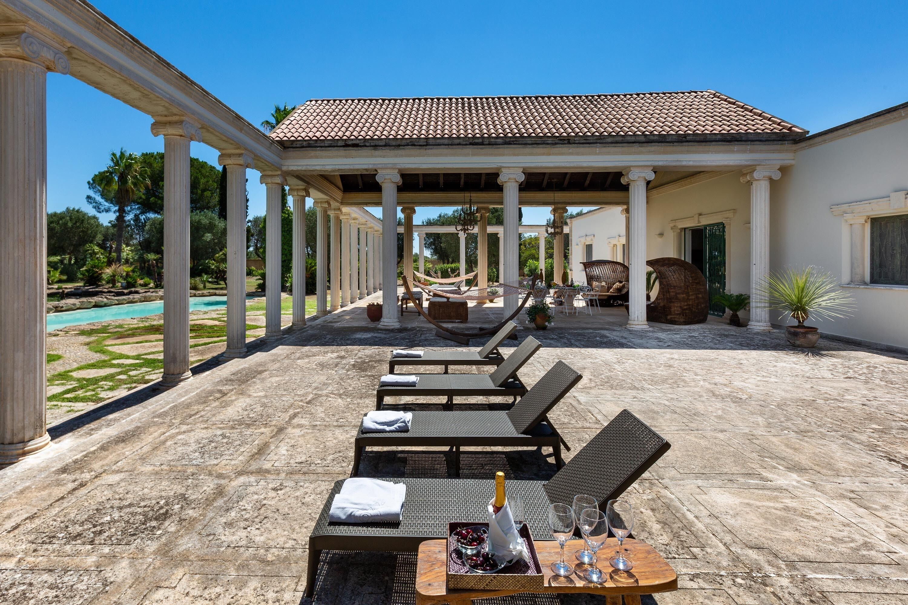 Een overdekt terras met lounge fauteuils en een tafel met een fles en glazen.